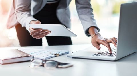 A business person checking holding a notebook in their right hand while typing with their left hand.